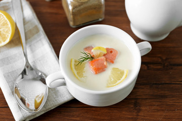 Delicious salmon cream soup on wooden table, which served with sliced lemon and spices