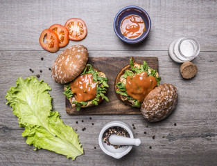 Ingredients for cooking a burger with chicken and vegetables, peppers, tomatoes, lettuce and salt on wooden rustic background top view close up