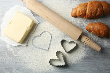 Heart of flour, croissant and  wooden kitchen utensils on gray background