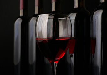 Red wine glass against bottles in a row on black background, close up