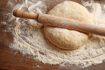 Dough for pizza and rolling-pin on wooden table