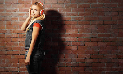 Young woman standing at the brick wall and listening to music