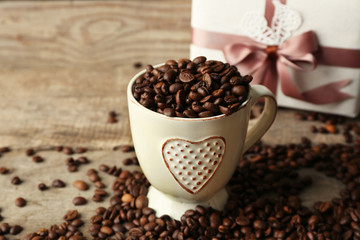 Beautiful gift with bow and coffee grains in mug, on wooden background