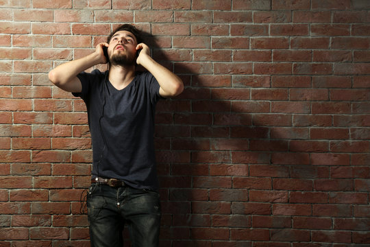 Young handsome man listening music with headphones on brick wall background