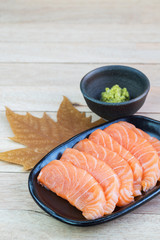 Sliced raw salmon on black plate with wood background
