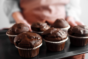 Housewife holding oven-tray with chocolate cupcakes, close up