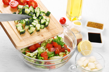Female hands adding vegetables  into bowl with salad, close-up