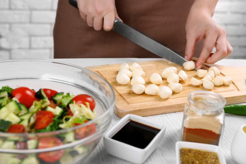 Female hands cutting mozzarella cheese for salad, at kitchen