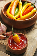 Colorful chili peppers in bowl and tasty sauce in bowl, on tray, close-up