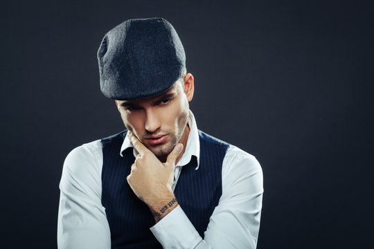 Handsome man in a vest and cap in studio on dark background