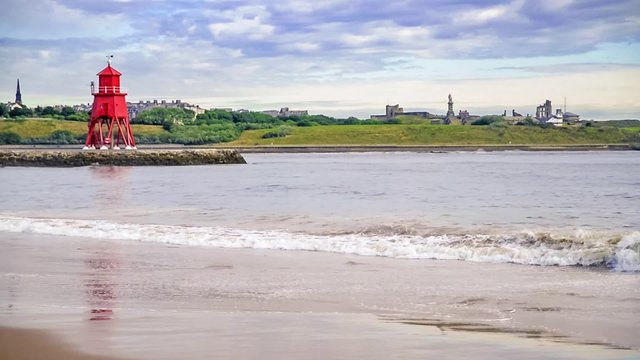 roter Leuchtturm an der Hafeneinfahrt von Newcastle Tyneside bei Sonnenaufgang, die Wellen laufen am Ufer aus
