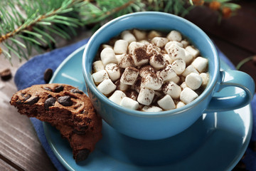 Mug of hot chocolate with marshmallows, fir tree branch on wooden background