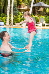 Naklejka premium Active father teaching his toddler daughter to swim in pool on tropical resort. Summer vacations and sport concept
