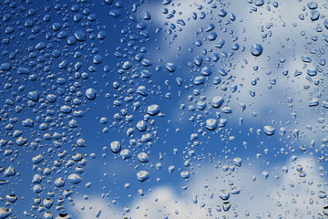 Rain drops on window with blue cloudy sky in background