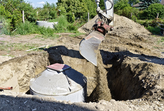 Bagger schüttet Material in Loch mit betonierter Senkgrube 