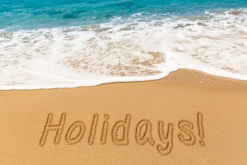 Holidays written in sand with sea surf