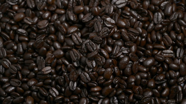 Hand drops some roasted coffee onto more beans.