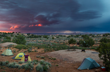 tents in a desert landscape with a dramatic pink and blue thunderstorm sky and arches national park in background - 98590773
