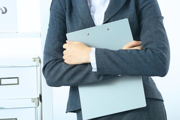 Attractive young businesswoman standing near desk with folder in the office