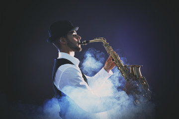 Elegant saxophonist plays jazz on dark background in blue smoke