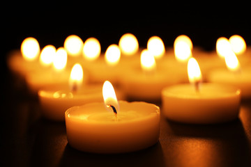 Fototapeta na wymiar Alight candles in a row on black background, blurred