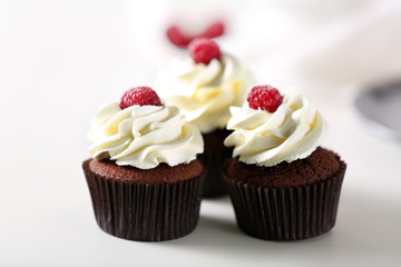 Beautiful chocolate cupcakes with cream and raspberry on table