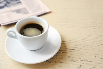 Cup of tasty coffee with newspaper on table