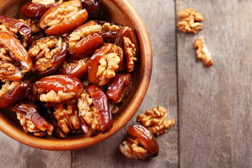 Walnut and date fruit in bowl on wooden table, close-up