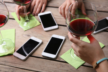 Four hands with smart phones holding glasses with red wine, on wooden table background