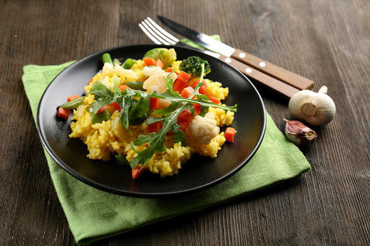 Black plate with vegetable risotto on served wooden table