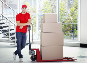 Delivery concept - postman in red uniform with parcels on dolly