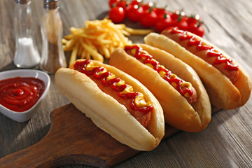 Tasty hot-dogs with French chips, spices and vegetables on wooden background