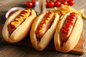 Tasty hot-dogs with French chips, spices and vegetables on wooden background, close up