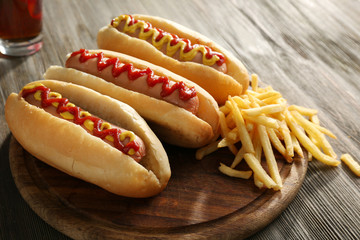 Delicious hot-dogs with French fries on wooden chopping board, close up