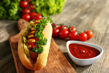 Delicious hot-dog with tomatoes and ketchup on wooden chopping board