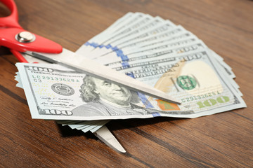 Red scissors cut money on wooden background. Financial concept