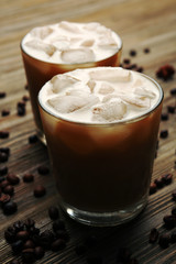 Two cups of ice coffee with coffee beans on wooden table
