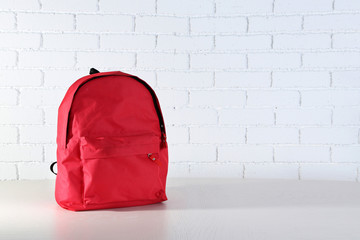 School backpack on wooden table, on wall background