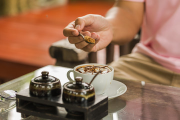 Closeup of a cropped man pouring sugar into coffee cup