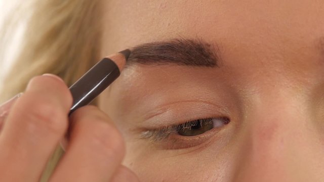 young girl draw beauty shape of eyebrows using cosmetic brush. Close up. Slow motion
