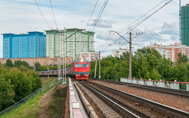 Obraz premium Red and grey suburban electric train moves towards on railroad turn vanishing against skyline background. Moscow, Russia. 