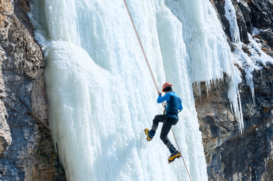 Climber going down the rope with a frozen waterfall