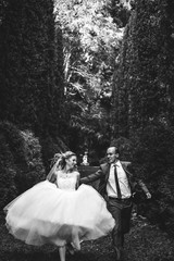 happy blonde bride  running and elegant groom on a background of beautiful sunny trees in  a forest