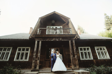 gorgeous stylish happy blonde bride and elegant groom near wooden cabin