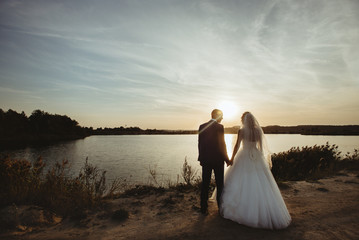 gorgeous stylish happy blonde bride and  elegant groom  looking at sunset