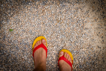 Close up of feet wearing yellow and red flip-flops on the stones