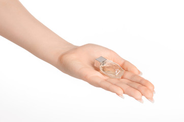 Perfume and body care theme: beautiful female hand holding a small transparent bottle of perfume on a white background isolated