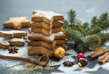 Cooked Christmas holiday traditional gingerbread cookies with sugar powder, anise and cinnamon sticks on black background