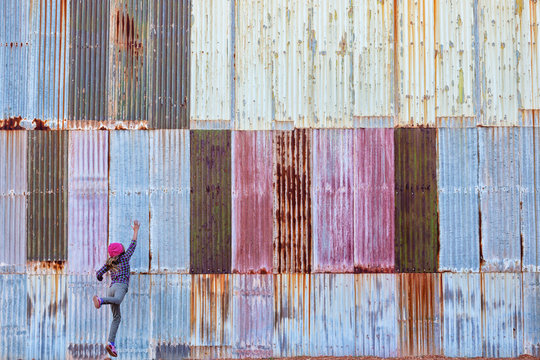 Girl jumping in front of a colorful corrugated metal wall, Kalgoorlie, Western Australia