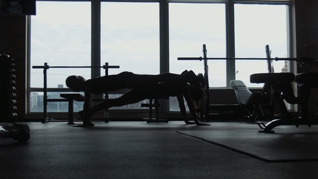 silhouette, two girls do push-ups together in a gym